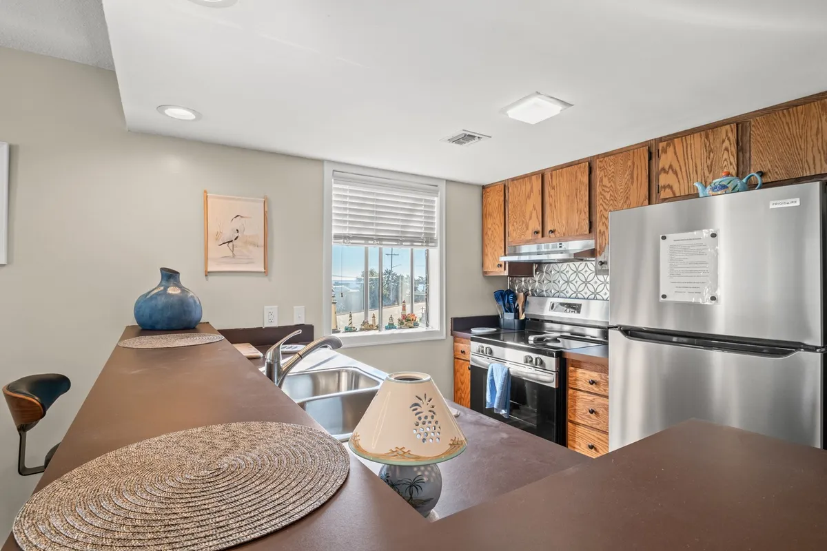A bright, modern kitchen featuring sleek stainless steel appliances, a spacious countertop, stylish cabinetry, a window offering natural light and a pleasant view, along with a decorative vase and neatly arranged kitchenware. The overall atmosphere is inviting and functional, perfect for both cooking and entertaining.