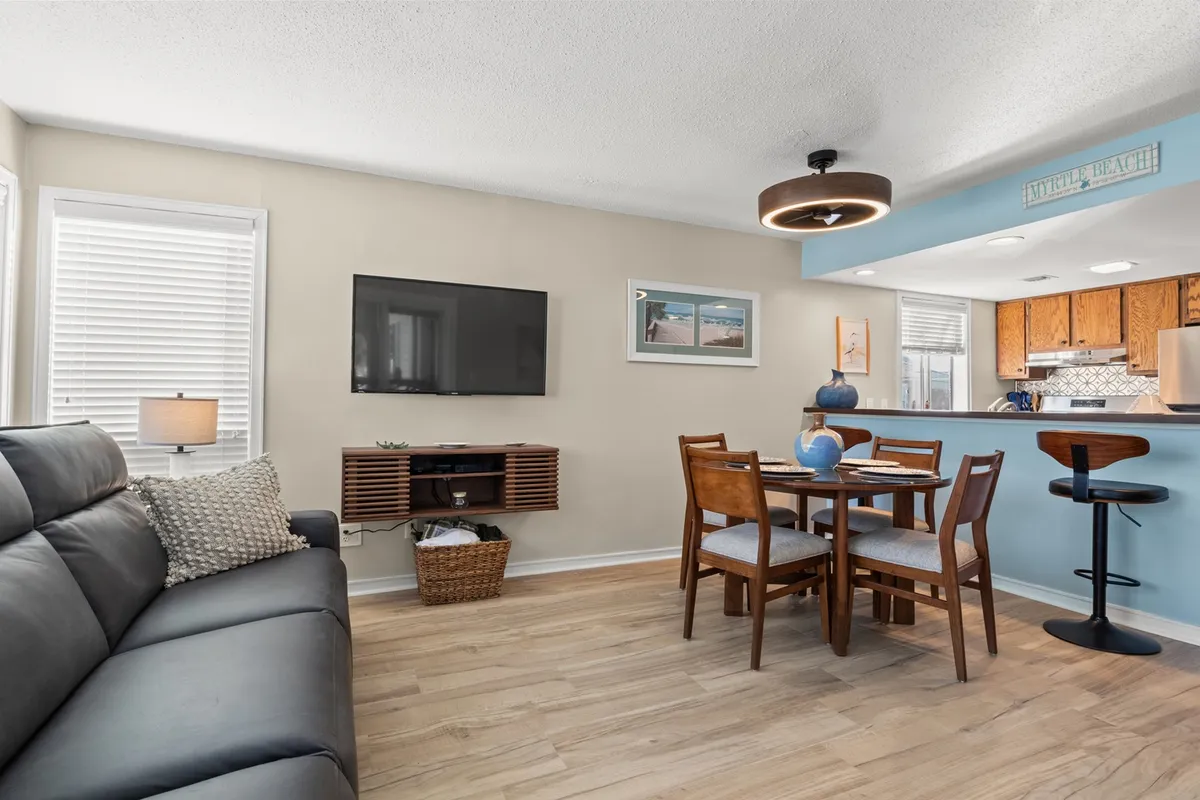 A cozy living space featuring a large sofa, a dining table ideal for group meals, a television for movie nights, and a kitchen bar area in the background. The arrangement is inviting for both relaxation and communal activities, with soft lighting enhancing the warmth of the room.