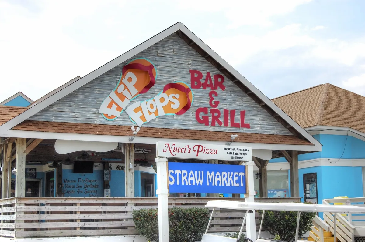 An exterior scene showcasing multiple restaurant and bar signs (Flip Flops Bar & Grill, Nucci’s Pizza, Straw Market) suggesting a cluster of casual dining and nightlife options. The mood is relaxed and cheerful, evoking a sense of local flavor and variety.
